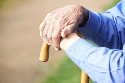 Elderly hands resting on a wooden cane outdoors.