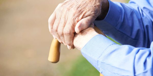Elderly hands resting on a wooden cane outdoors.