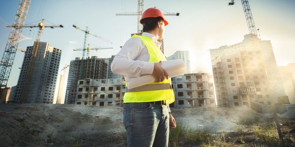 Construction worker with plans overseeing building site at sunset.