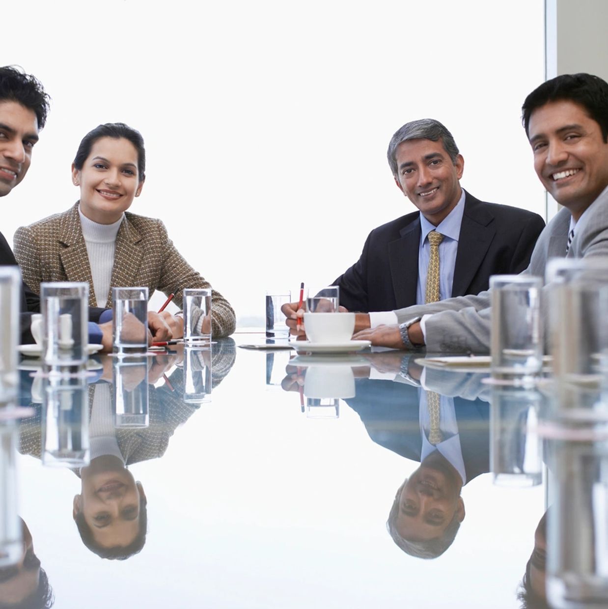 Four professionals smiling around a glass table in a meeting room.