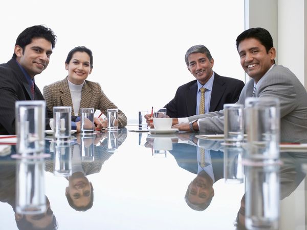 Four professionals smiling around a glass table in a meeting room.