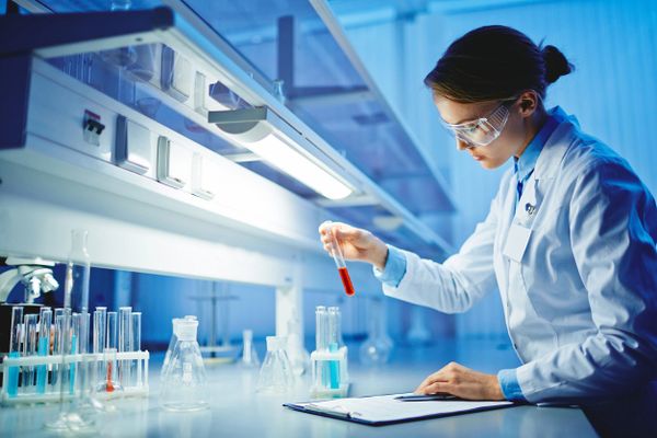 Scientist in lab coat examining a red liquid in a test tube.