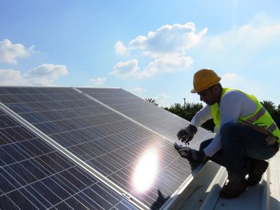 Worker installs solar panels on a sunny day, wearing safety gear.