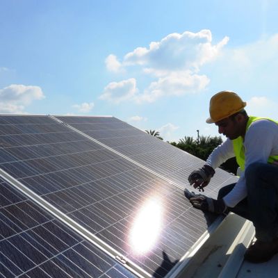 Technician installing solar panels on a rooftop under clear skies.