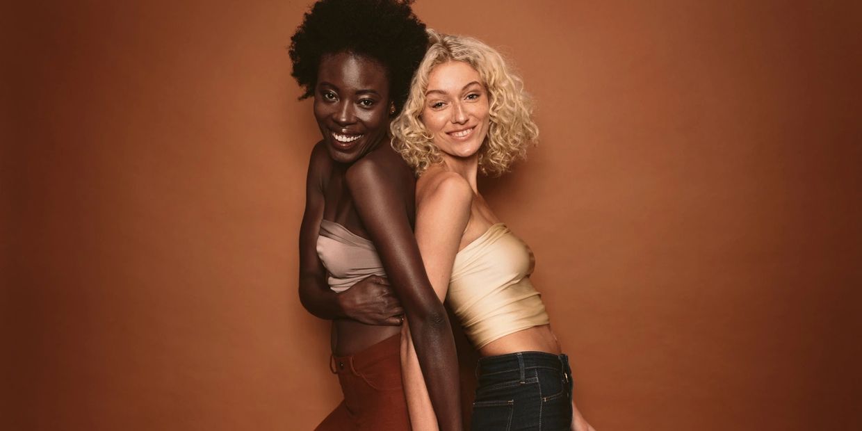 Two women smiling and posing back to back against a brown background.