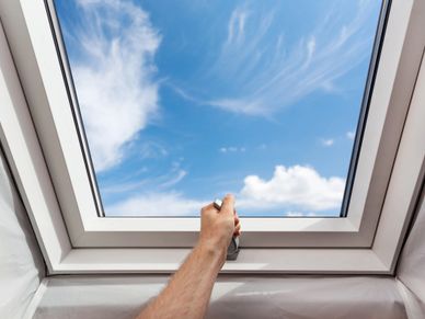 Hand opening a skylight window to a bright blue sky.