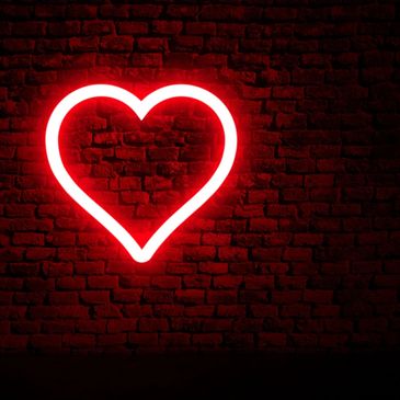 Red neon heart glowing on a dark brick wall.