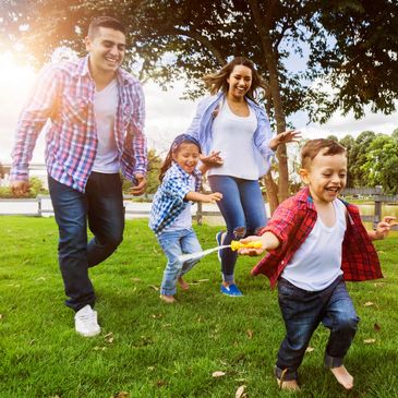 Family joyfully playing with a skipping rope in a sunny park.