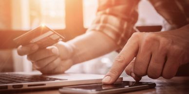 A person pays a bill. They are holding a debit card and typing on a phone. 