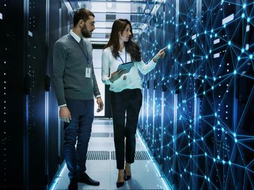 Two IT professionals collaborate inside a high-tech data center, analyzing network infrastructure 