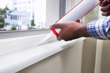 Person applying sealant on a window sill for weatherproofing.