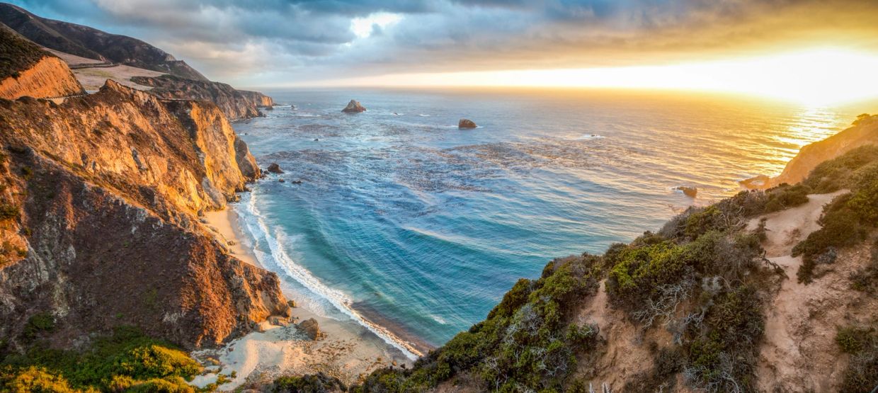 Sunset over rocky coastline with waves.