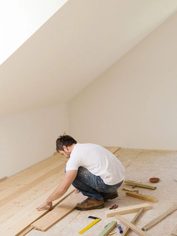 Man applying wood flooring with a slanted wall in the background