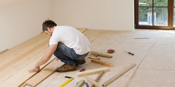 Man installing wooden flooring in a bright room.