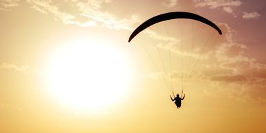 A person paragliding against a bright sunset sky.