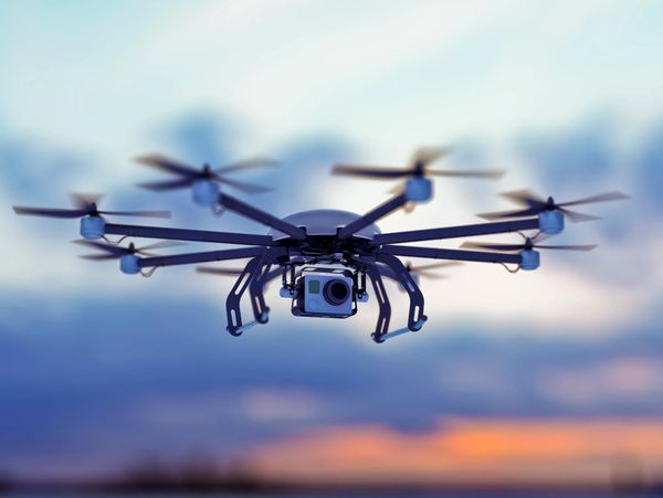 A professional octocopter drone flying with a mounted camera at sunset.