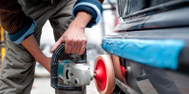 Man is using a power buffer to make the paint shine on a black car.