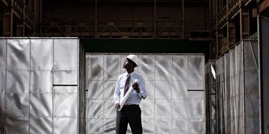 Man in formal attire standing confidently in an industrial setting.