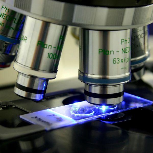 Close-up of microscope lenses focusing on a slide under blue light.