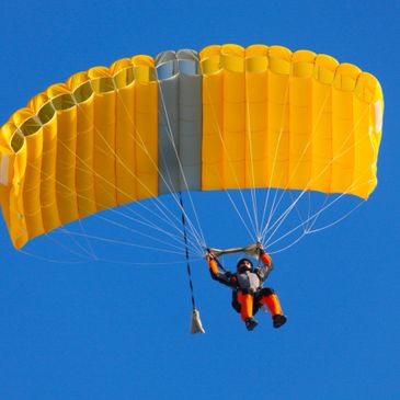 Person descending with a bright yellow parachute against a clear blue sky.