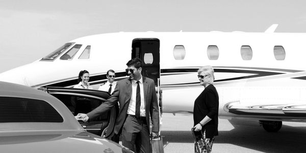 A couple of business travelers getting inside of their private car after getting of a personal jet.