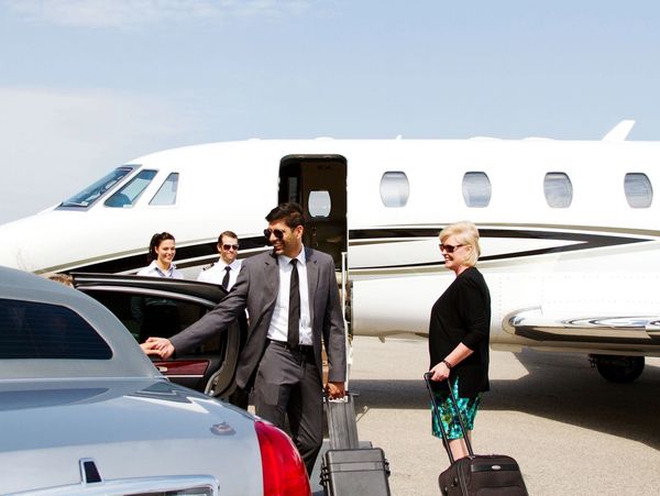 Business travelers arriving at a private jet, greeted by pilots and a chauffeur.