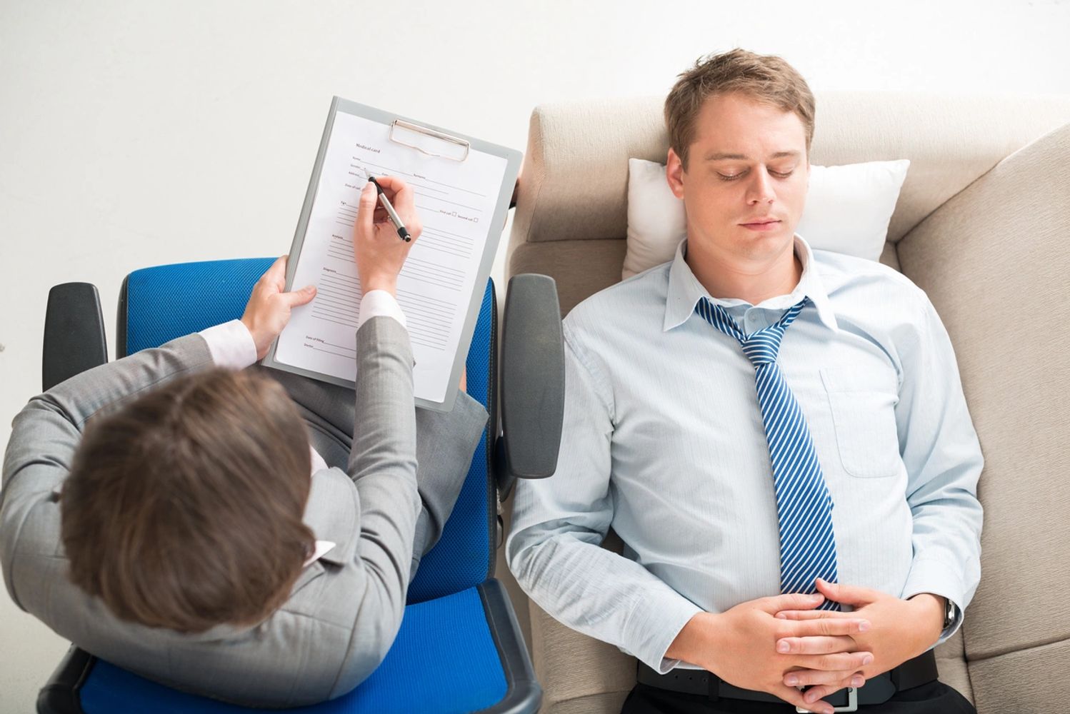 Man lying on a couch during a therapy session with a psychologist taking notes.