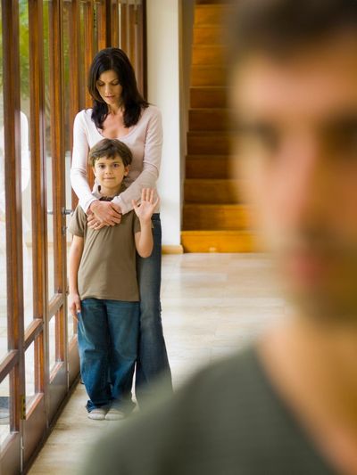 Mother standing behind  her son with her arms around the child.