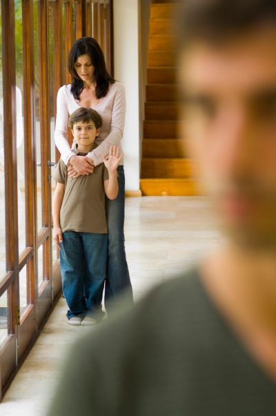 Woman hugging boy who waves, with blurred man in foreground.
