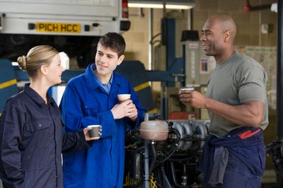Three mechanics chatting and drinking coffee in a garage.