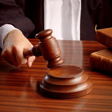 Judge's hand striking a wooden gavel on a sound block in a courtroom.
