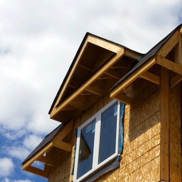 Partially constructed house with exposed wooden framing under a blue sky.