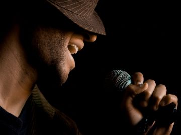 Person singing into a microphone with a hat on.