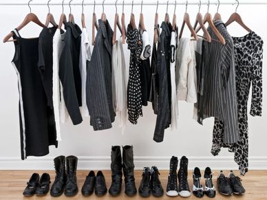 Black and white clothing on hangers with various shoes below.