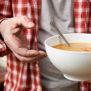 volunteer hands a hot bowl of delicious looking soup to at guest at a community meal