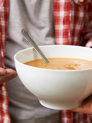 Person holding a bowl of soup with a spoon.