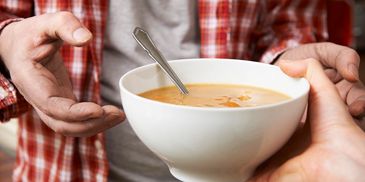 Person holding a bowl of soup with a spoon.