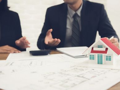 Two people discussing real estate plans with a house model and blueprints.