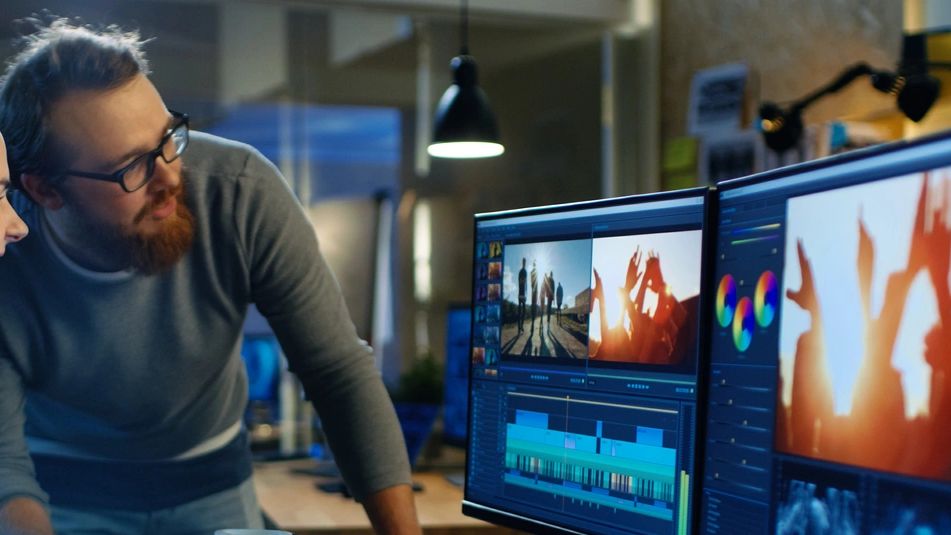 Two people editing video on dual monitors in a modern workspace.