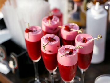 Six champagne flutes filled with a strawberry cocktail and candy garnish.
