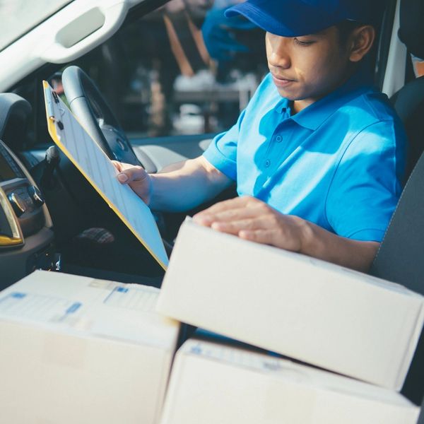 Courier in blue uniform checking delivery details inside a vehicle with packages.