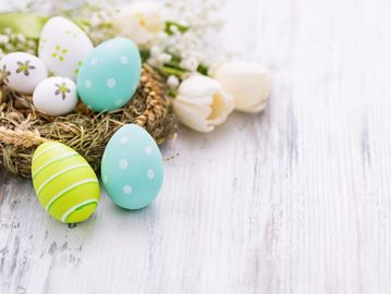 Colorful decorated Easter eggs in a nest with white flowers on a wooden surface.