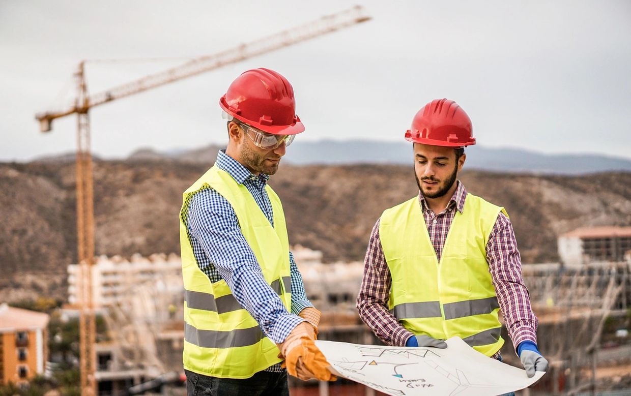 Two construction workers reviewing blueprints at a building site.
