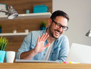 Man waving and smiling during a video call at home.