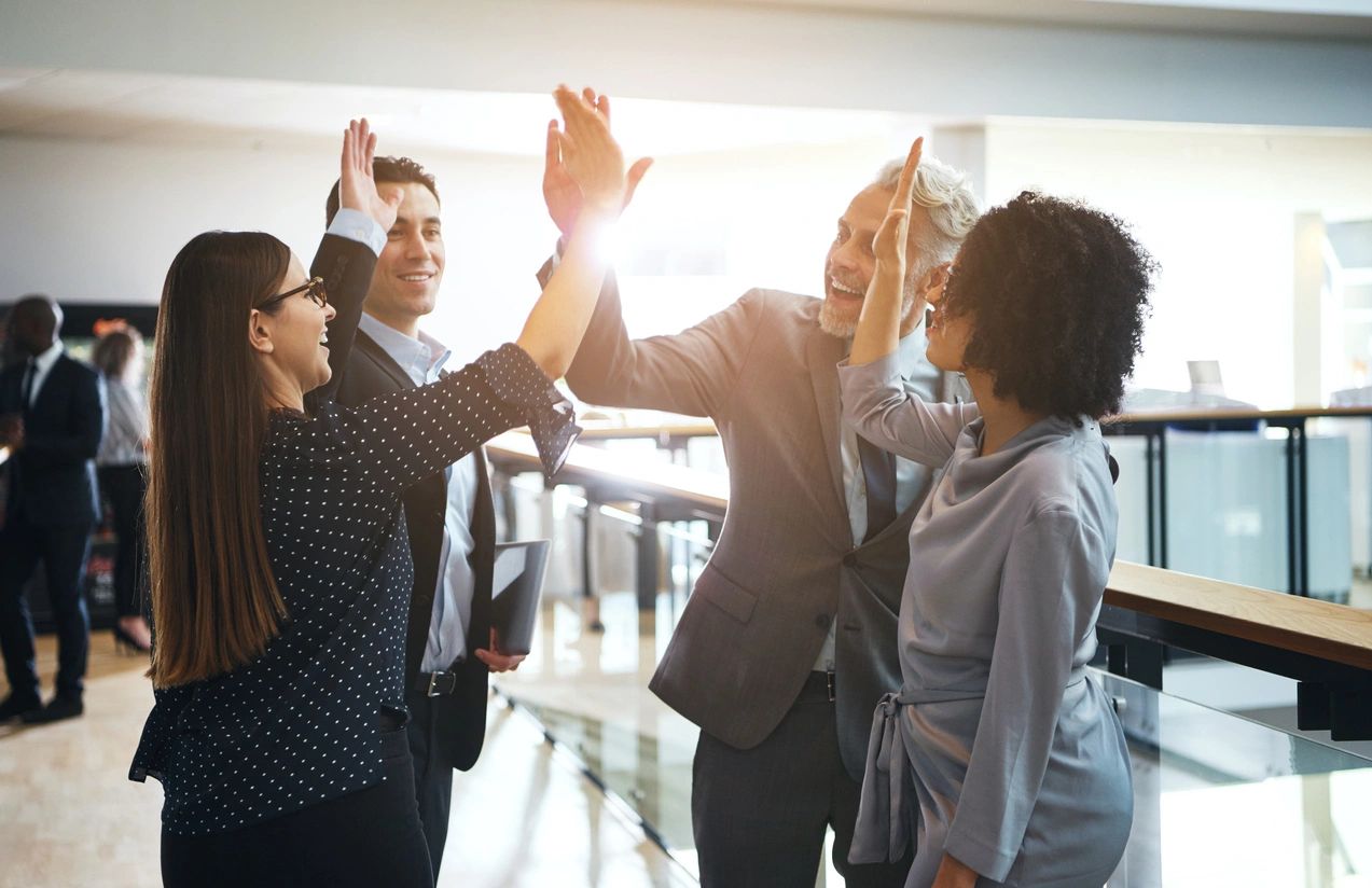 A business team celebrates their win with a collective high-five amongst the four of them.