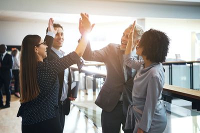 A group of people in an office setting, standing, smiling and giving high fives. 