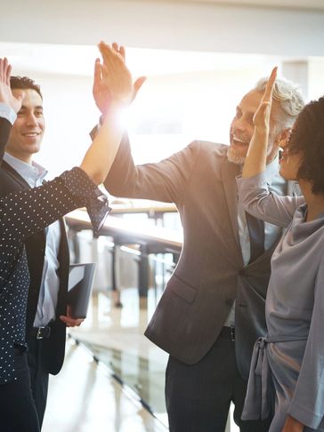 Colleagues enthusiastically giving high-fives in a bright office setting.