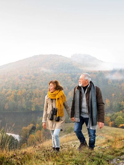 Ein altes Ehepaar spaziert über einen Berg und im Hintergrund ist ein Wald mit Nebel zu sehen