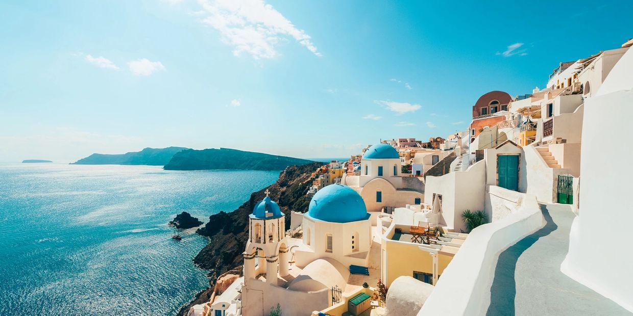 Sunny view of Santorini with blue-domed churches by the sea.