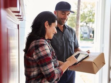 Woman signing on a tablet as delivery man hands over a package.